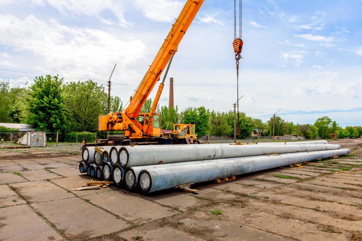 Descarga de postes de hormigón de alta tensión en el sitio de construcción con una grúa elevadora foto