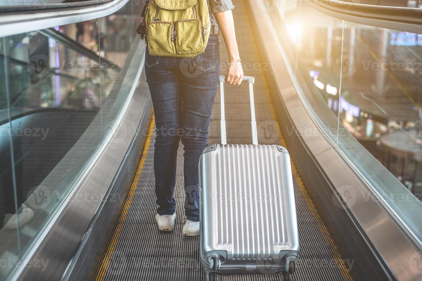 Vista posterior de la mujer de belleza viajando y sosteniendo la maleta en la escalera mecánica foto