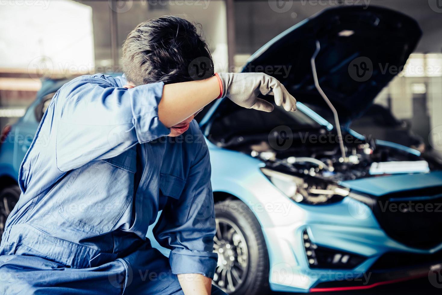 Car mechanic resting from exhaustion and wiping sweat from tired photo