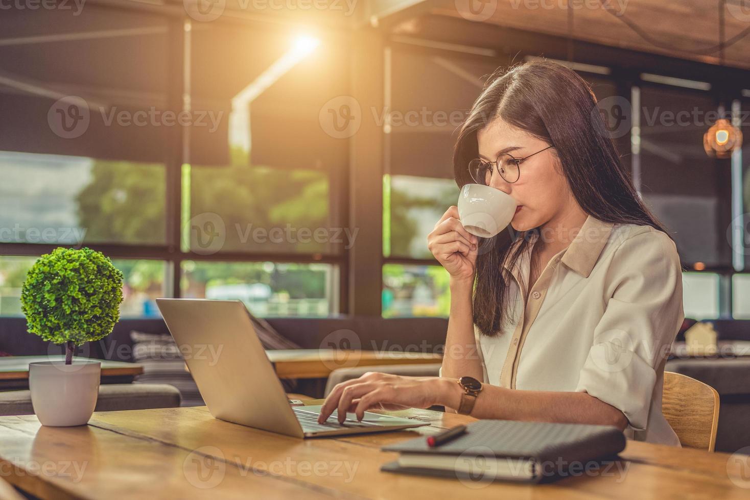 Mujer trabajadora asiática con ordenador portátil y tomando café en la cafetería foto