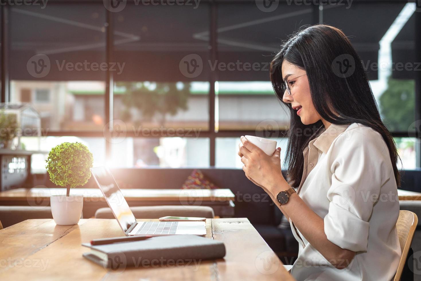 Mujer trabajadora asiática con ordenador portátil y tomando café en la cafetería foto