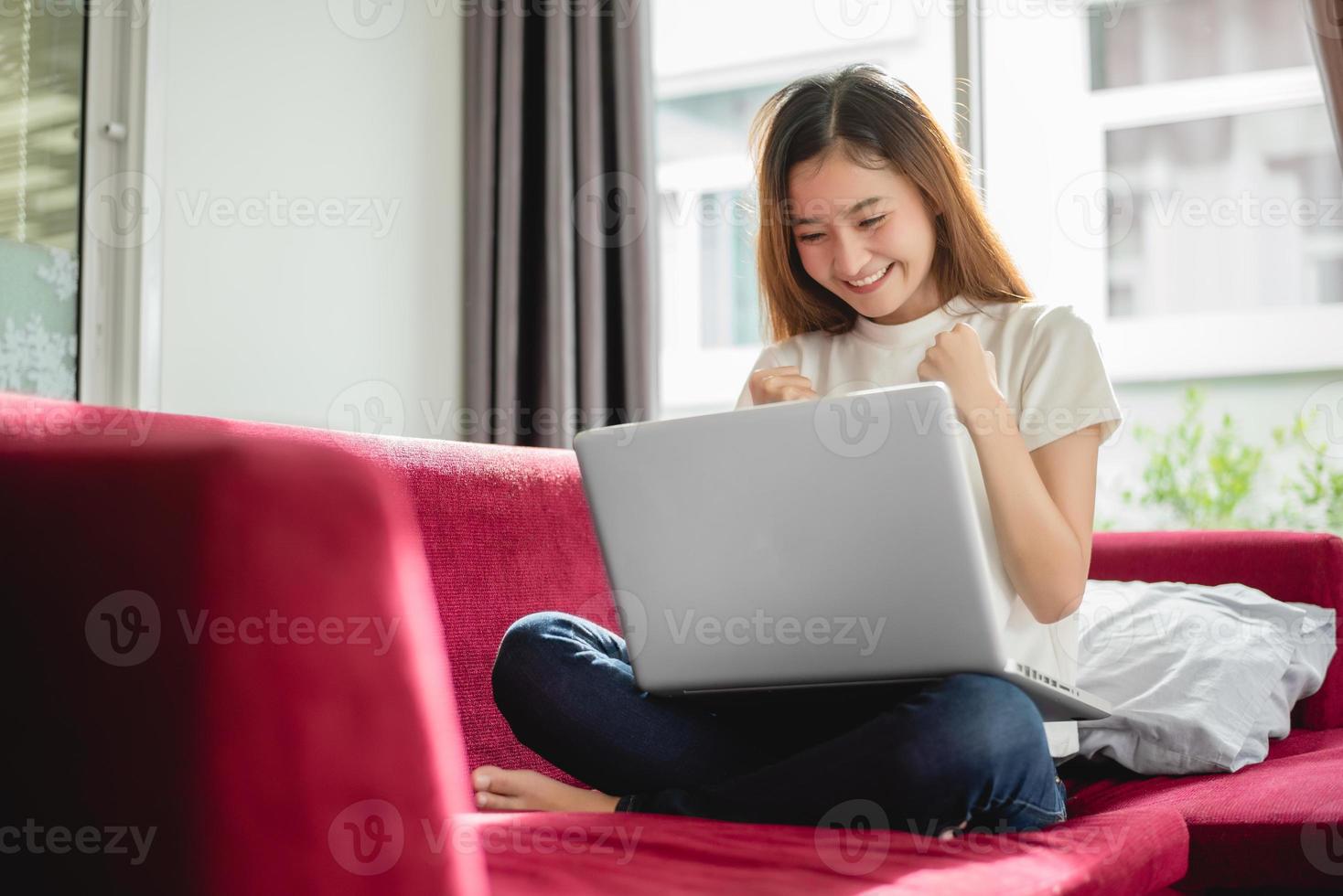 Young woman surfing the internet by laptop on red sofa photo