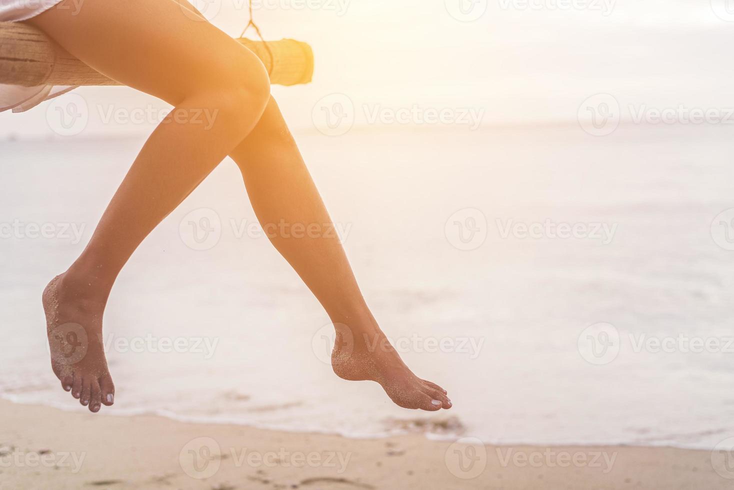 Piernas de mujer en la playa en columpio de madera foto