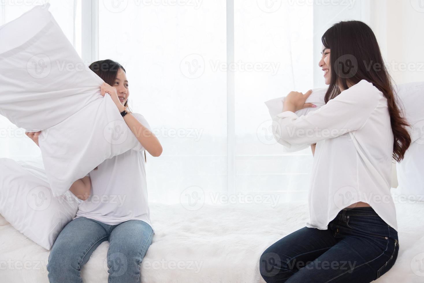 Dos chicas asiáticas haciendo pelea de almohadas en el dormitorio como infancia foto