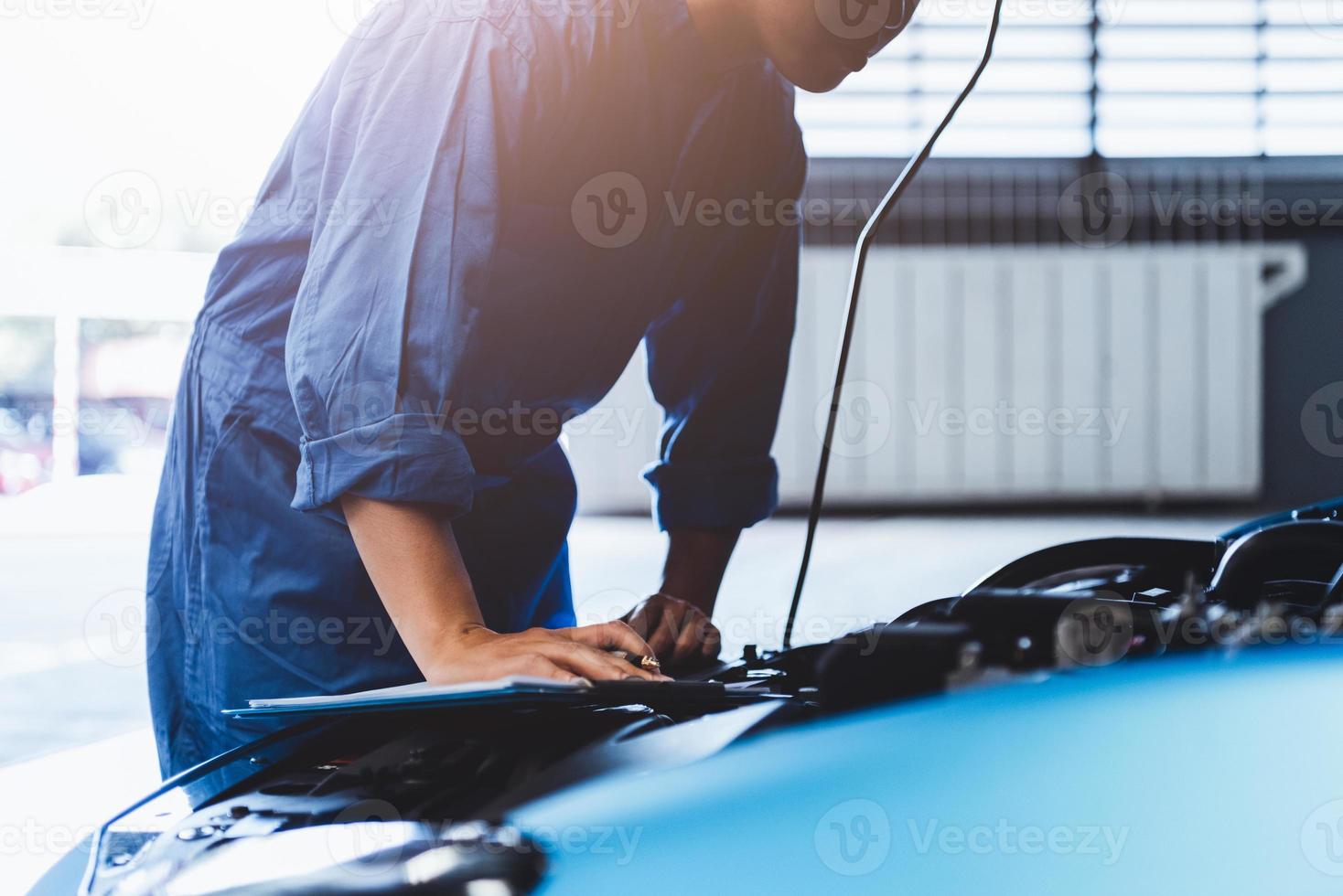 mecánico de automóviles sosteniendo el portapapeles y comprobando el vehículo de mantenimiento foto