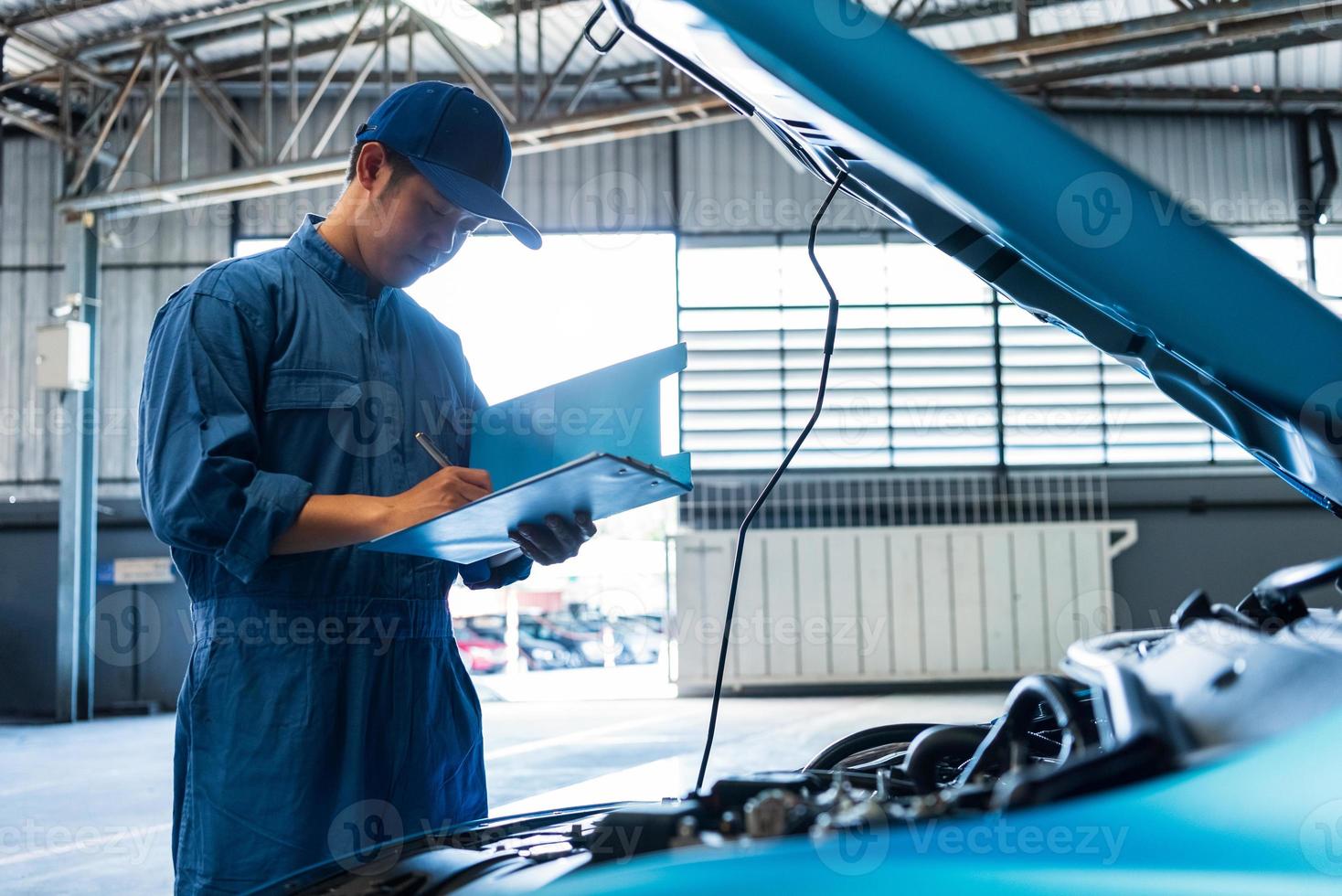 mecánico de automóviles sosteniendo el portapapeles y comprobando el vehículo de mantenimiento foto