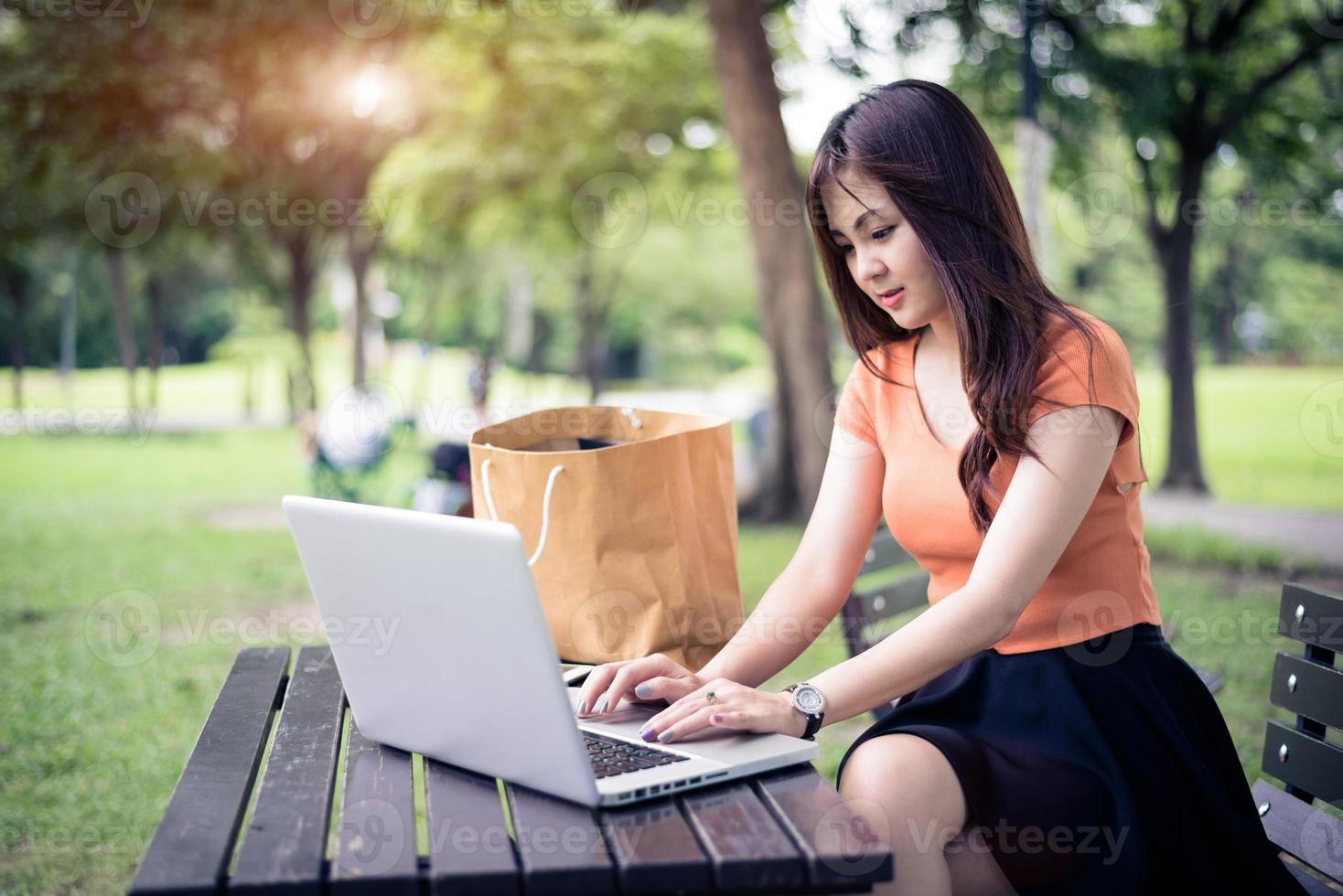 Asian woman using and typing on laptop keyboard in outdoors park photo