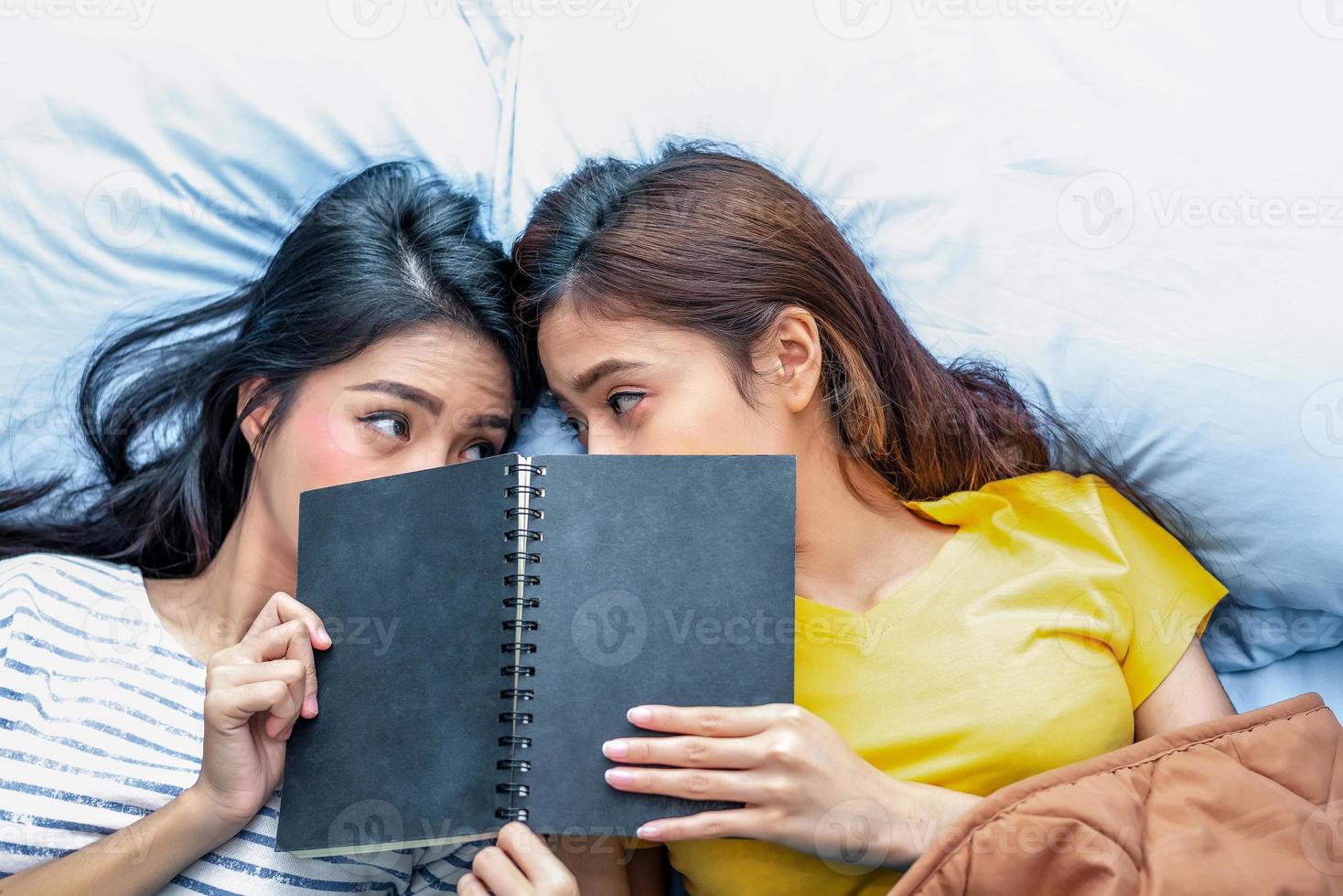 Cute Asian lesbian couple reading book together and lying on bed photo