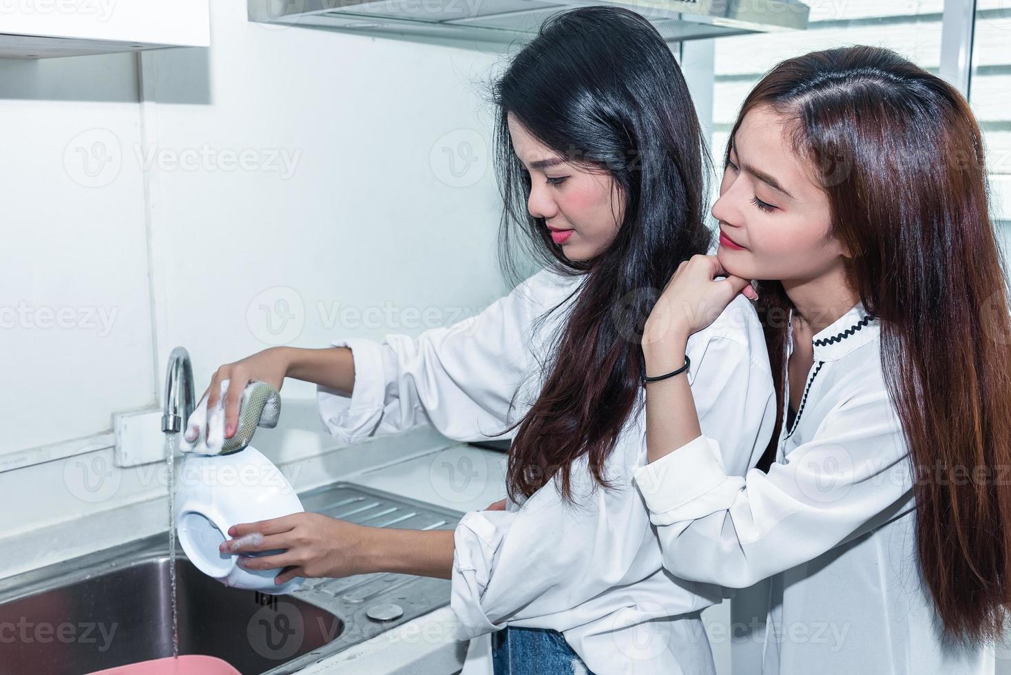 Two Asian women washing dishes together in kitchen photo