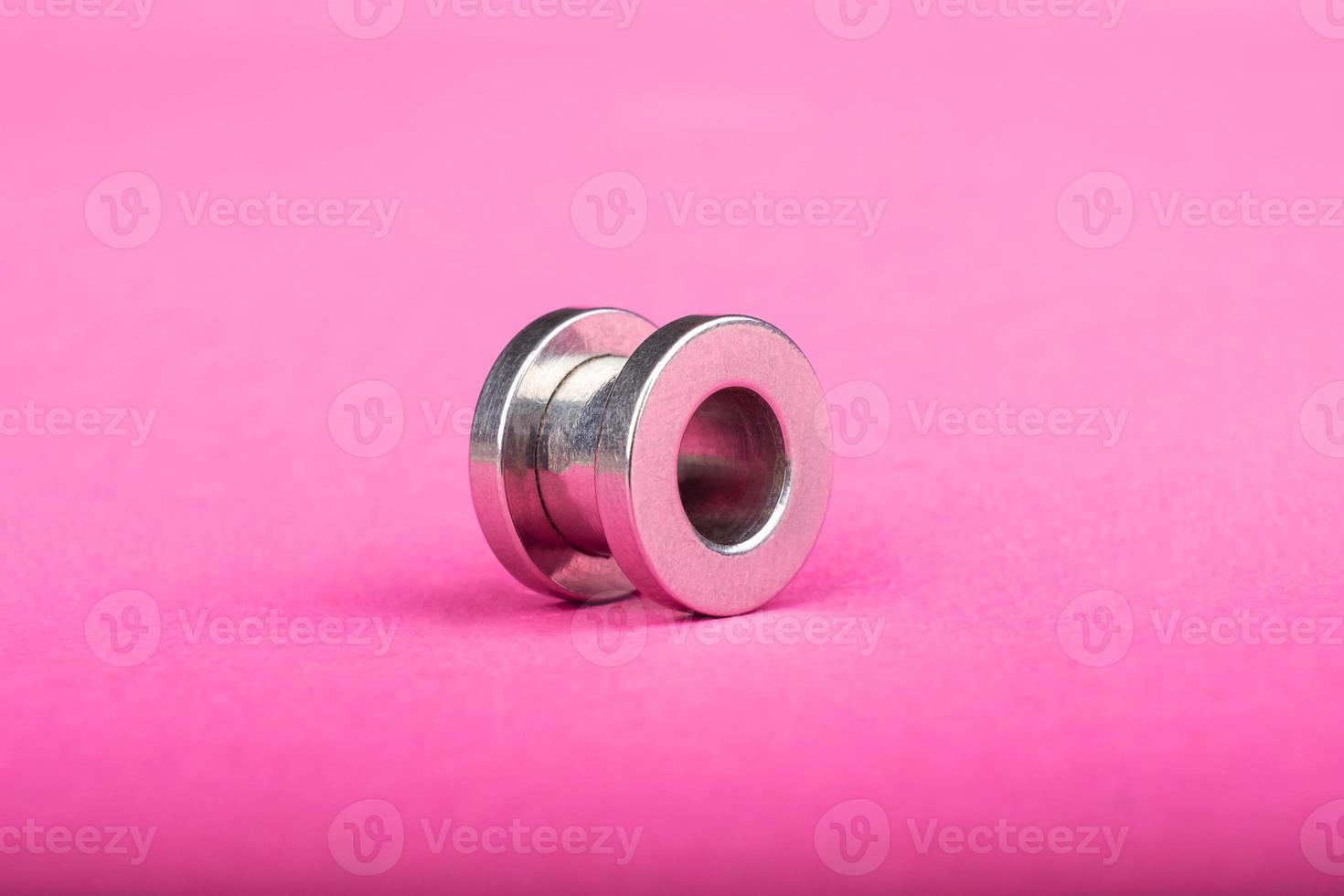 piercing, silver ear tunnel on pink background close-up photo