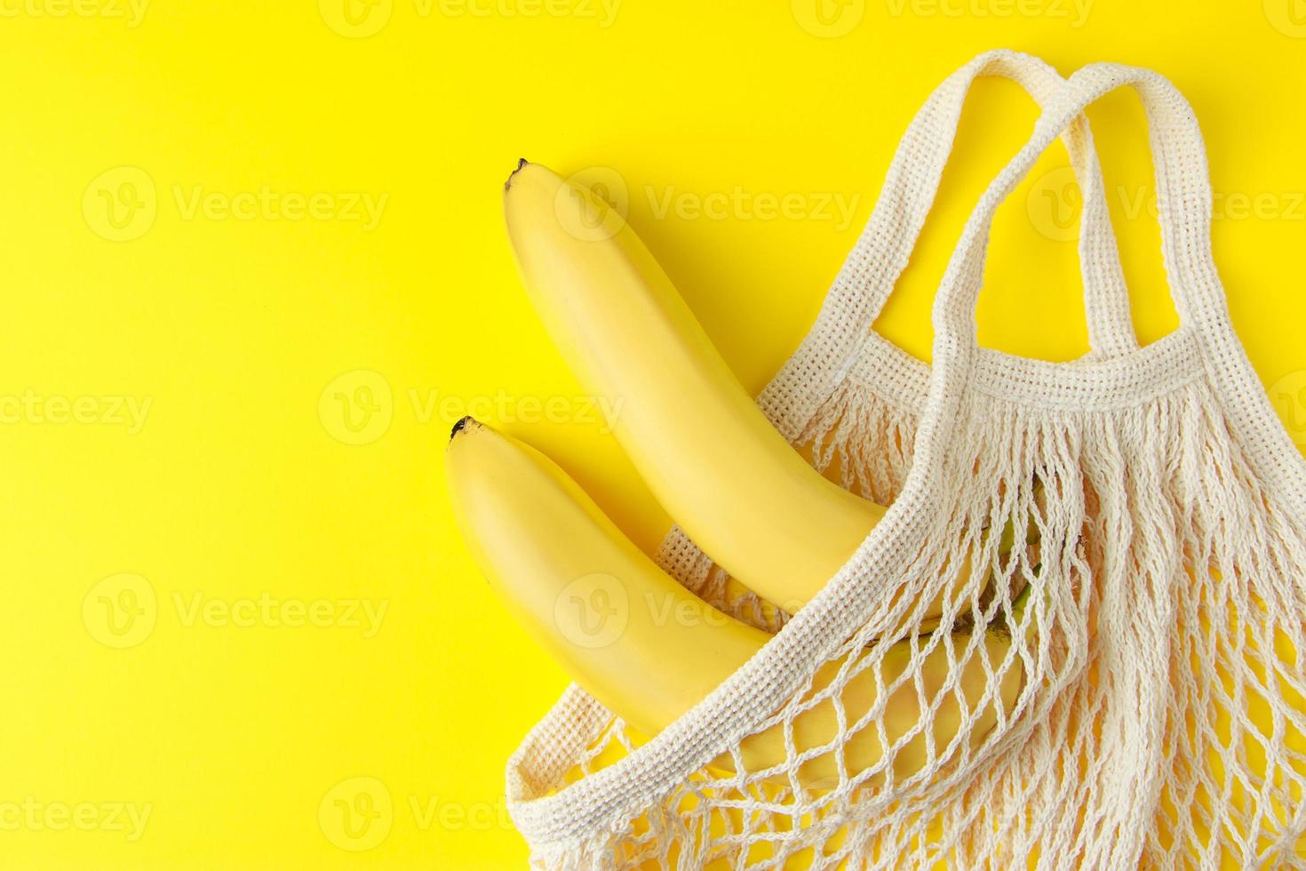 Ripe bananas in mesh bag on yellow background. Eco shopping bag. photo