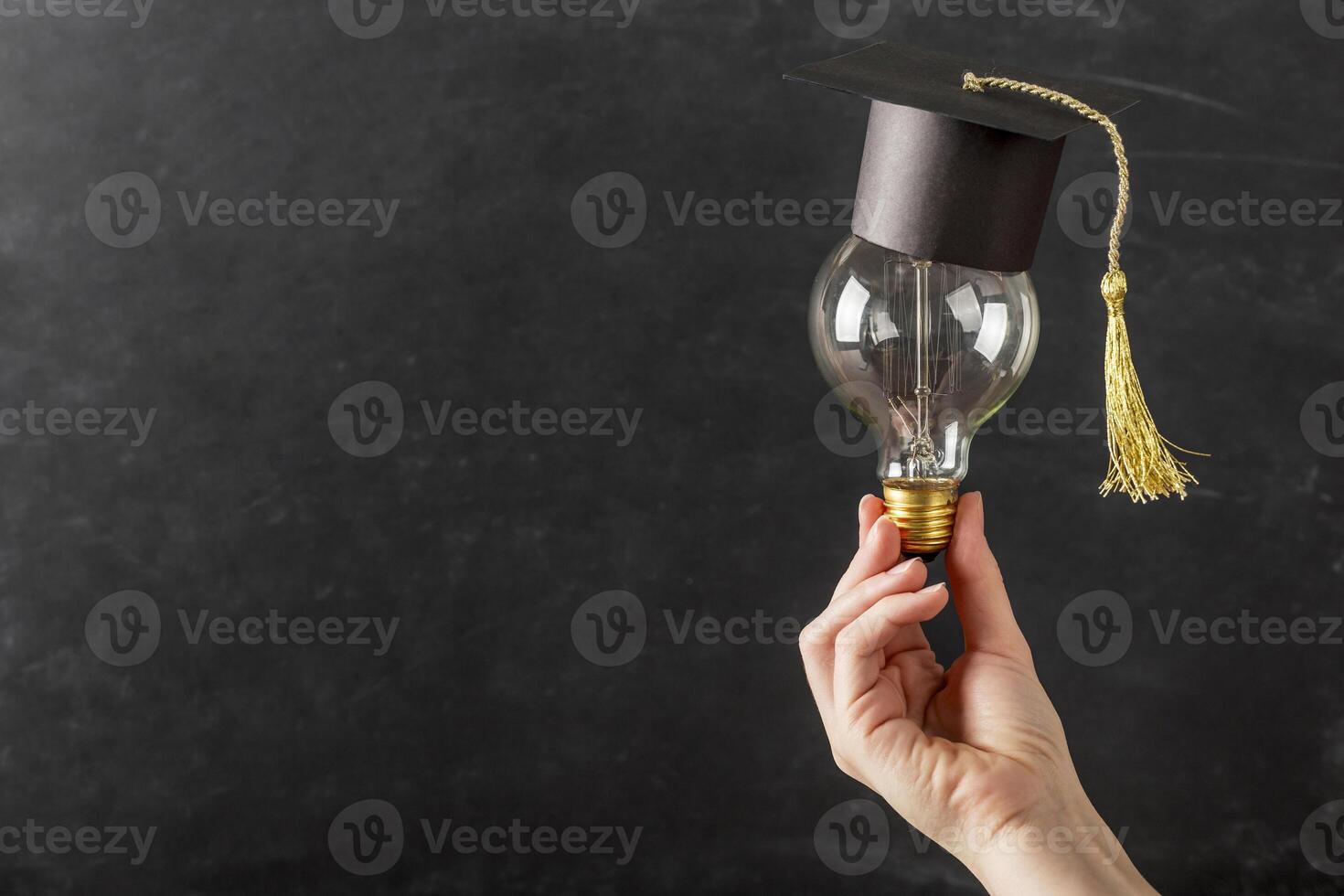 persona sosteniendo bombilla con gorro de graduación foto