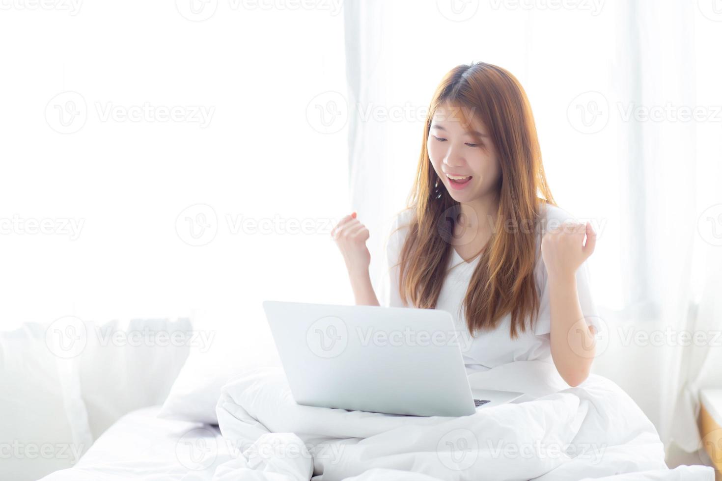 Young asian woman using laptop work with success on bed. photo