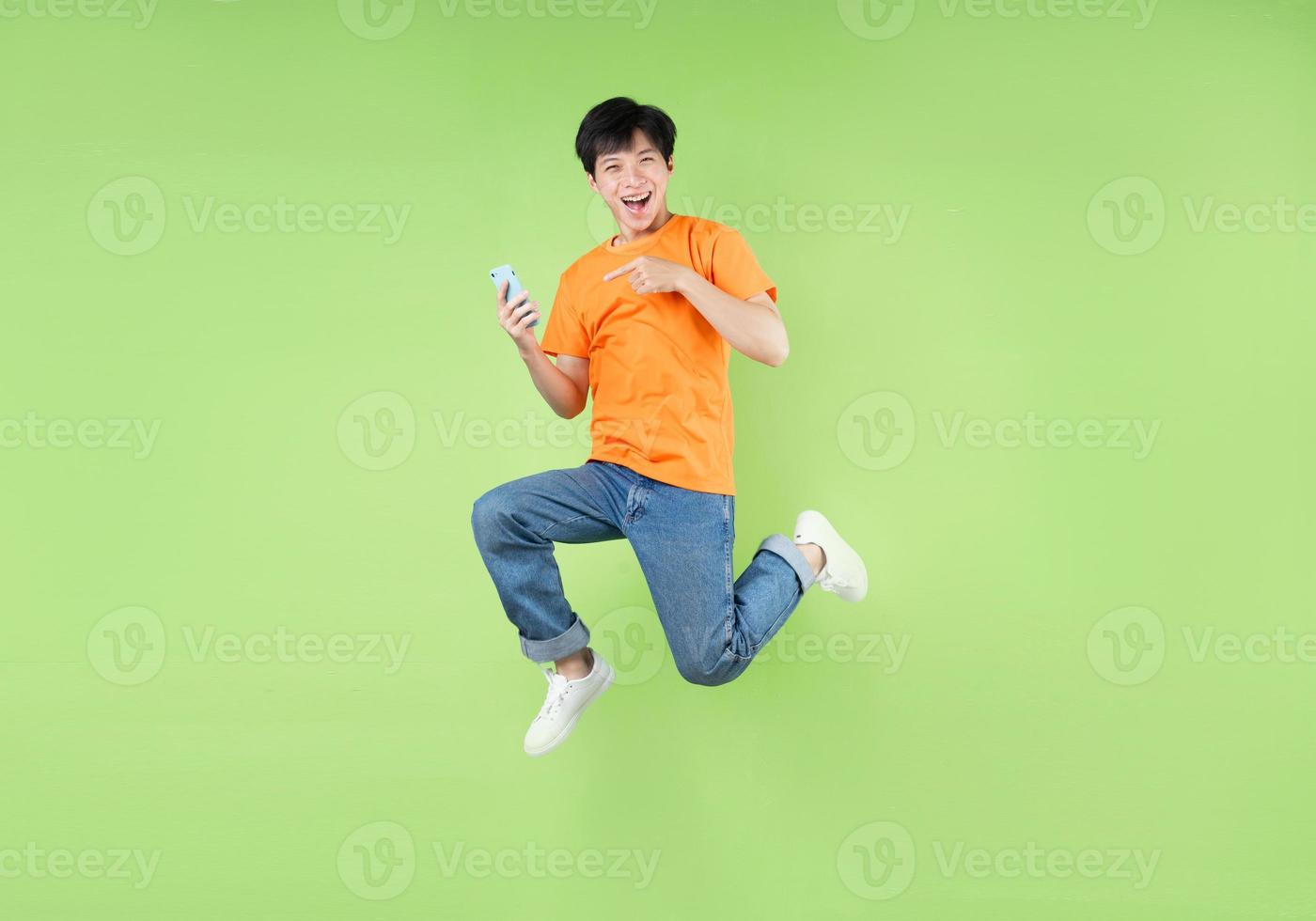 Asian man jumping and holding smartphone , isolated on green photo