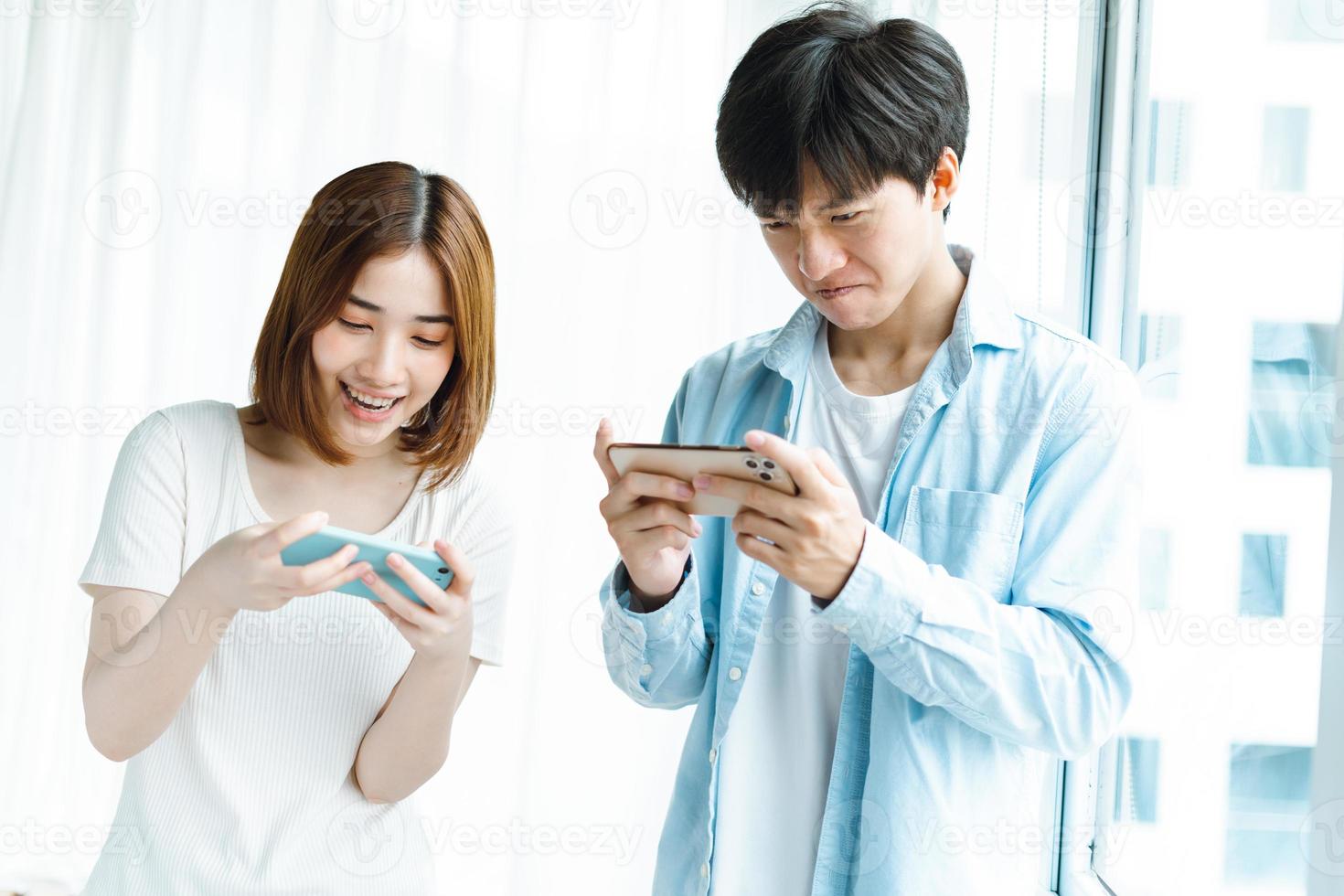 Young Asian couple playing games together on mobile phones photo