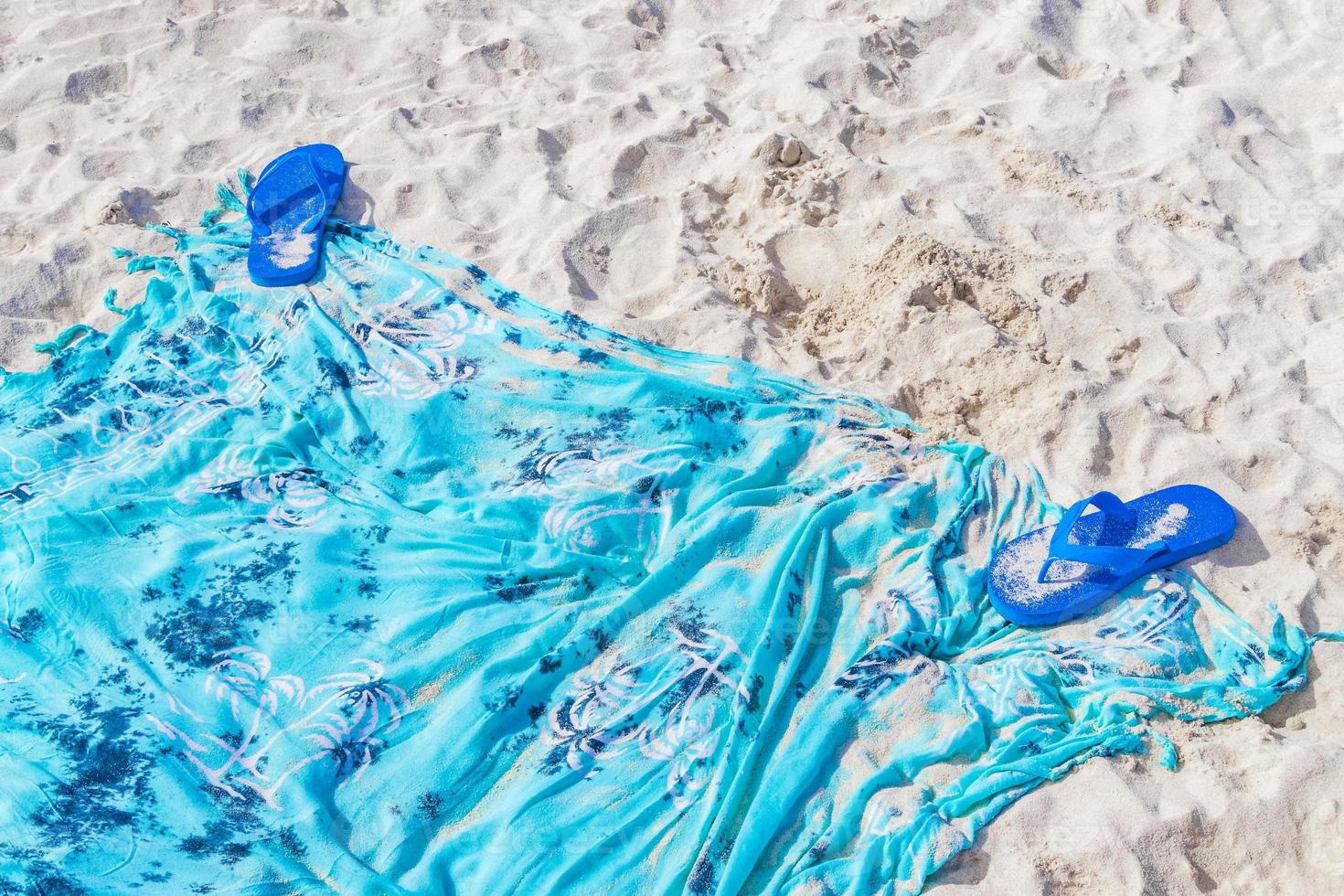 Blue flipflops on blue beach blanket towel on white sand. photo