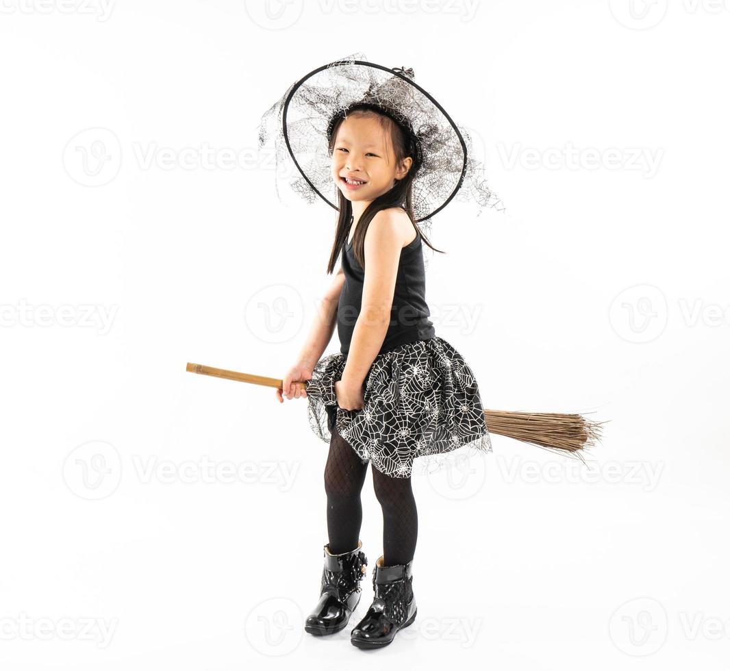 Retrato de niña asiática vestirse de bruja montando la escoba foto