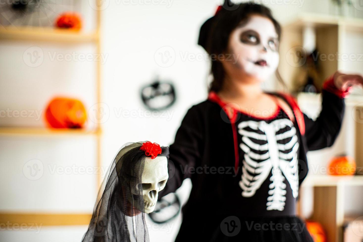 Blurred portrait Asian little girl in Halloween costume holding skull photo