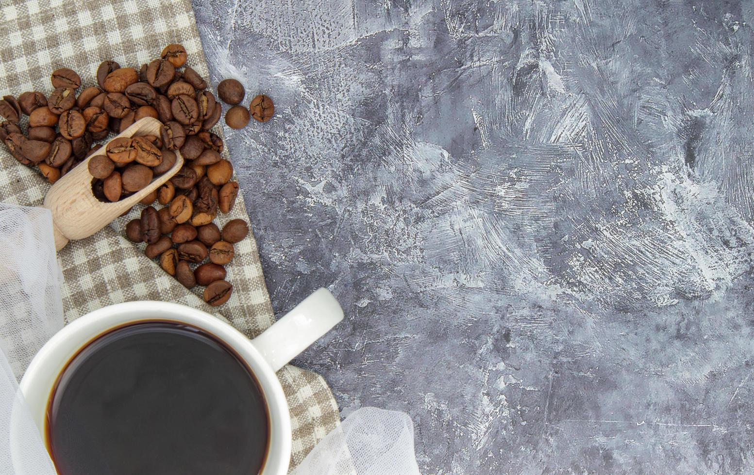 taza blanca de café negro americano, mantón de tela con granos de café foto