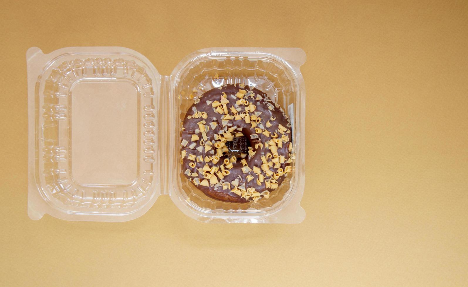 Chocolate donut in a plastic container on a brown or coffee background photo
