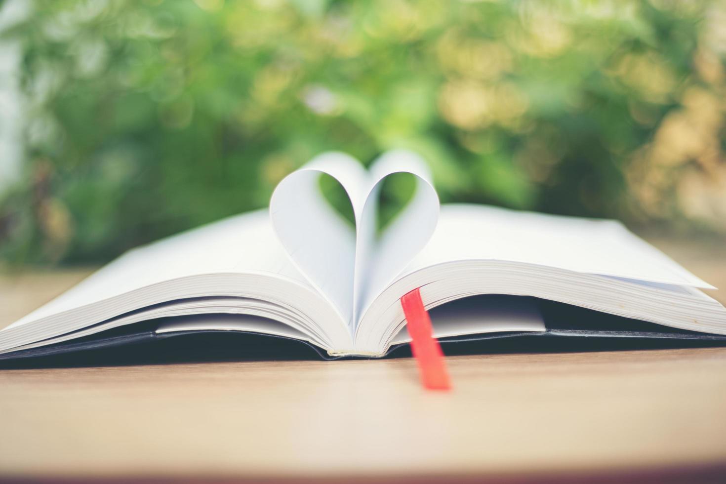 Open book on wooden table on natural background. Heart book page photo