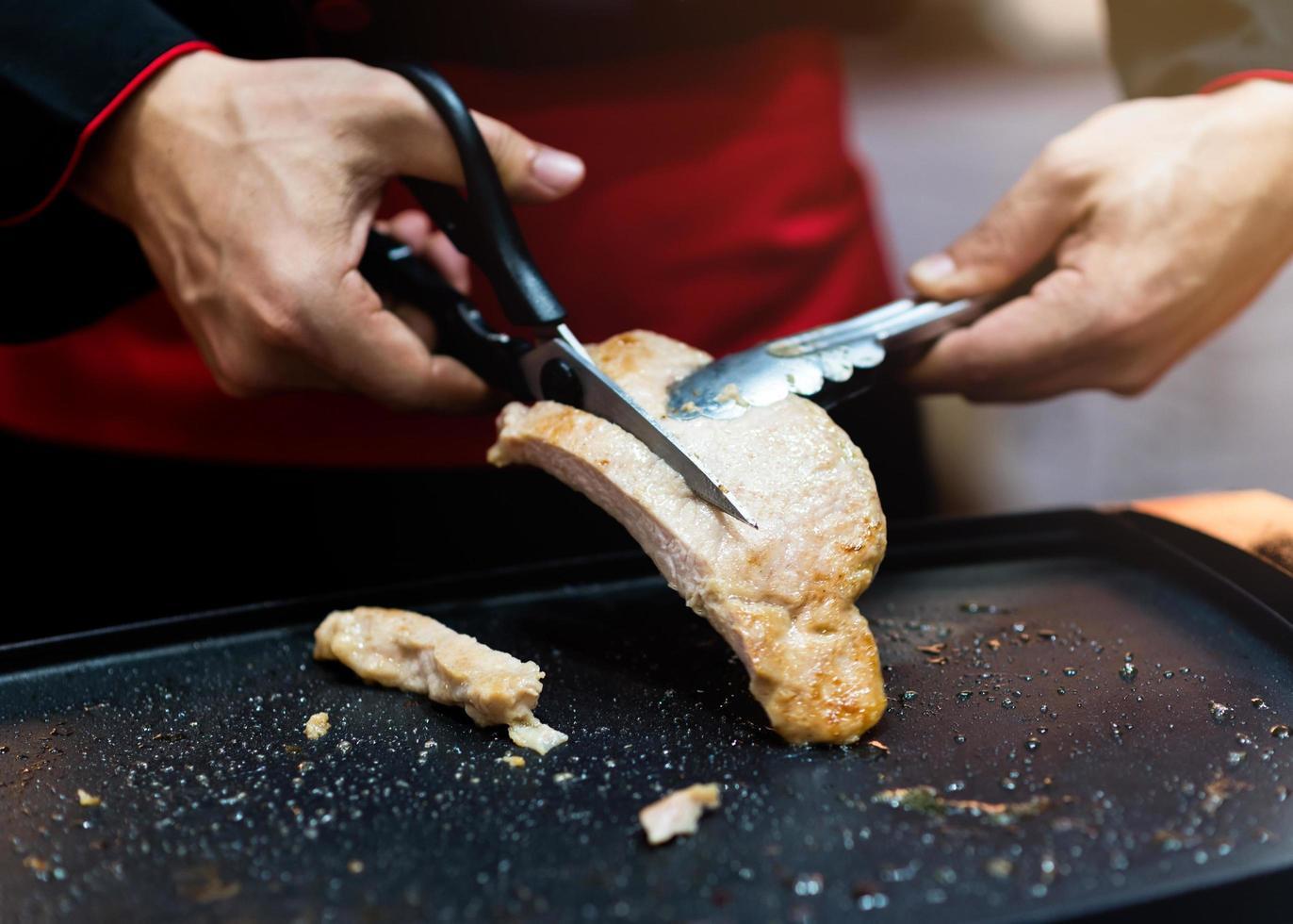 Asimiento de la mano tijeras cortando filete de cerdo a la parrilla foto