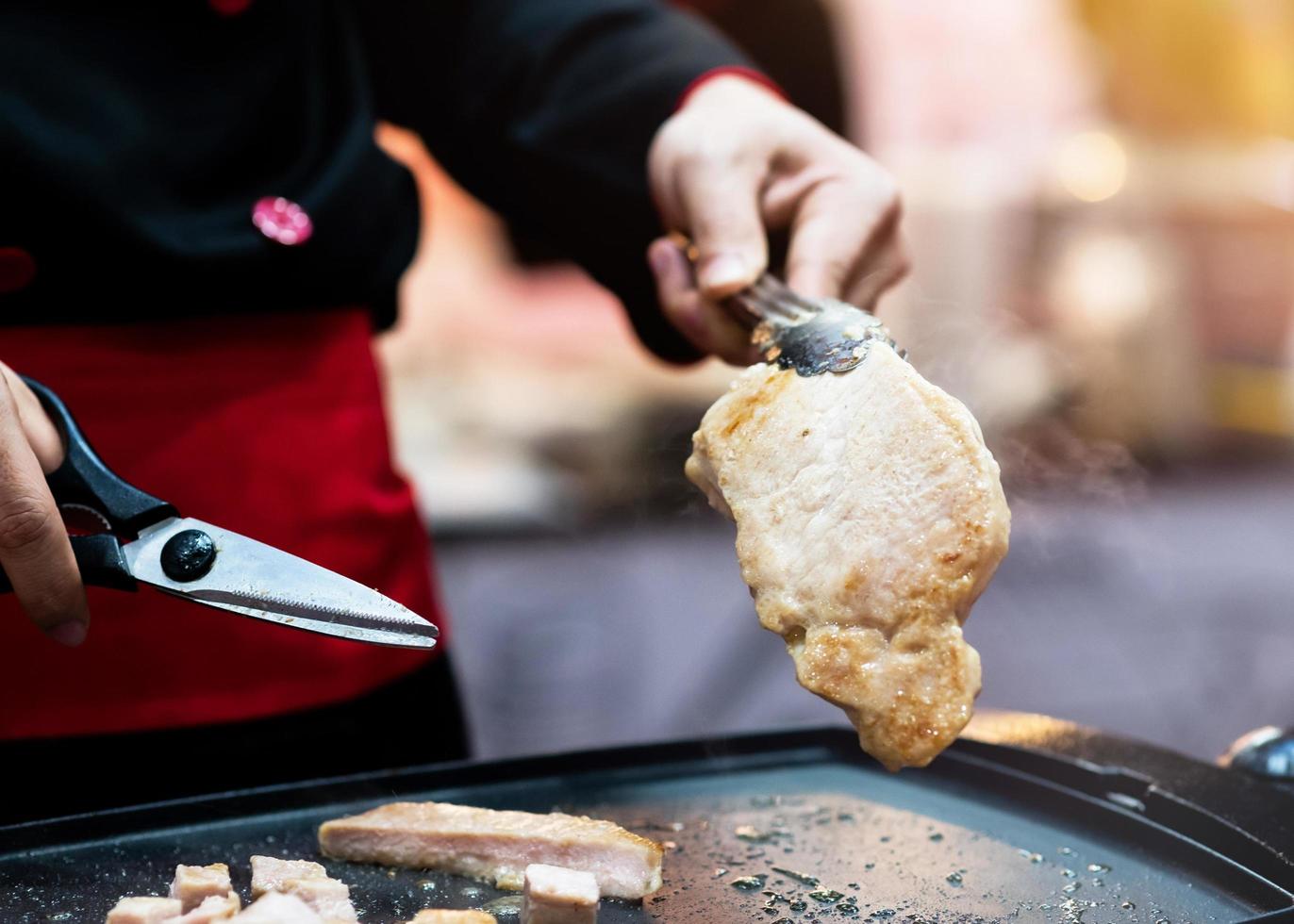 Asimiento de la mano tijeras cortando filete de cerdo a la parrilla foto