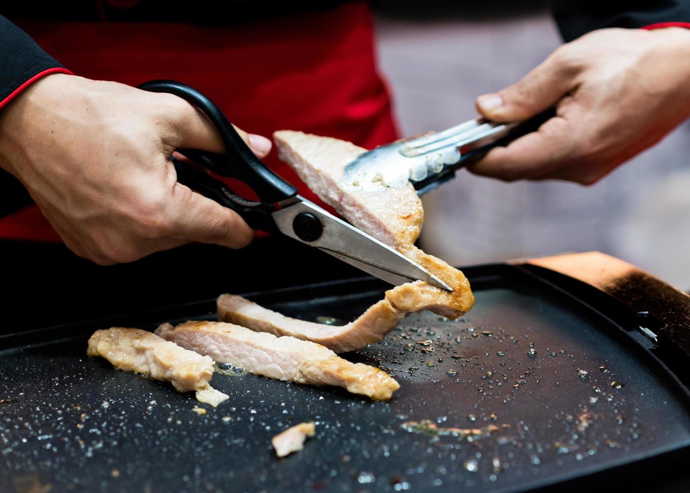 Asimiento de la mano tijeras cortando filete de cerdo a la parrilla foto