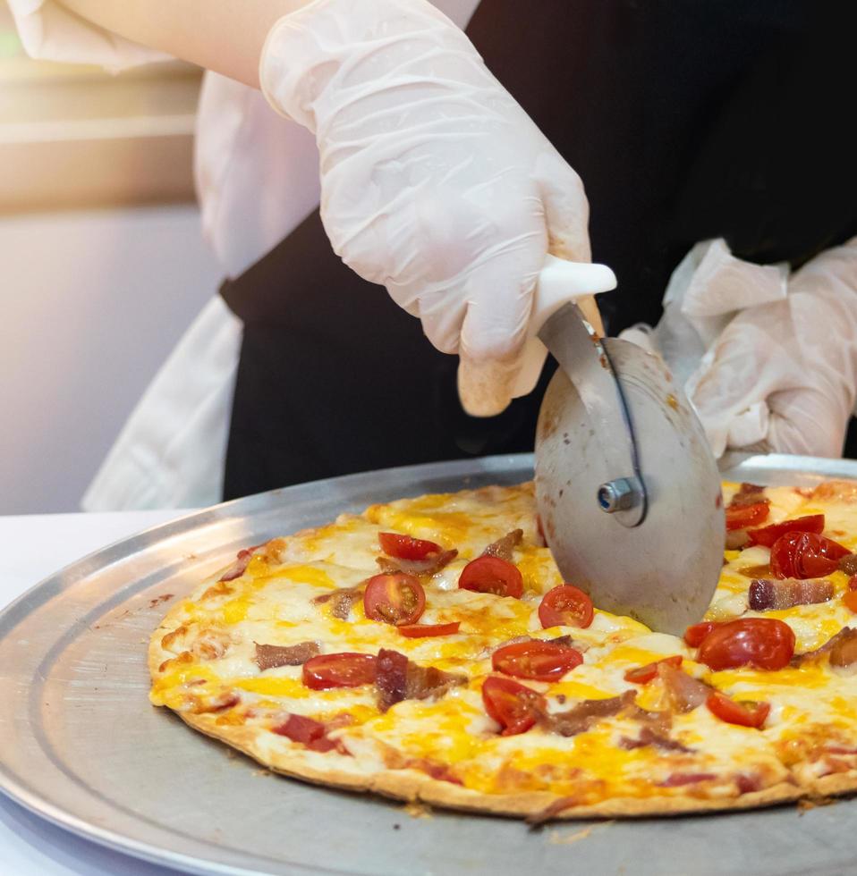 Primer plano de la mano del chef cortando pizza en la cocina foto