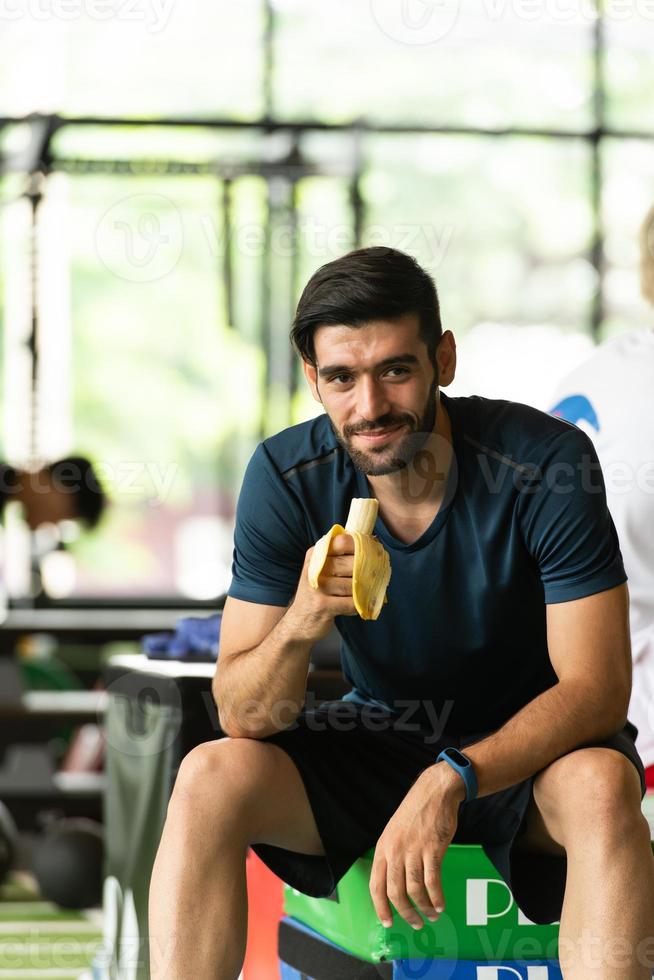 Young man work out at the gym and eating bananas before exercise. photo