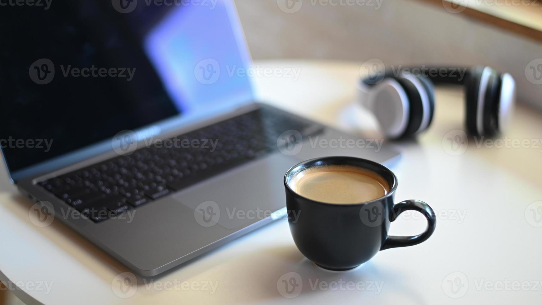 taza de café con portátil borrosa y auriculares colocados sobre una mesa. foto