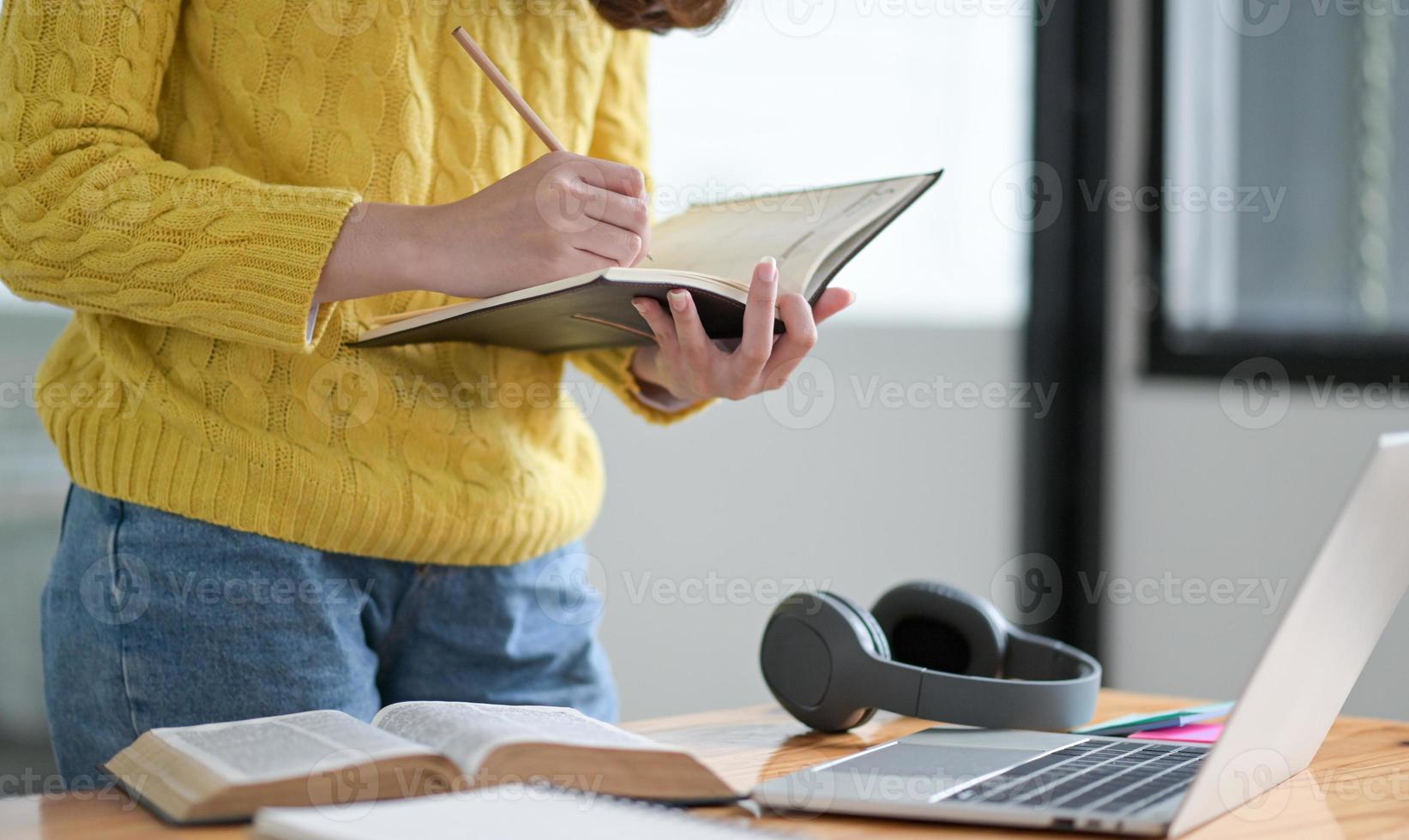 una estudiante toma notas en un cuaderno durante una clase en línea. foto