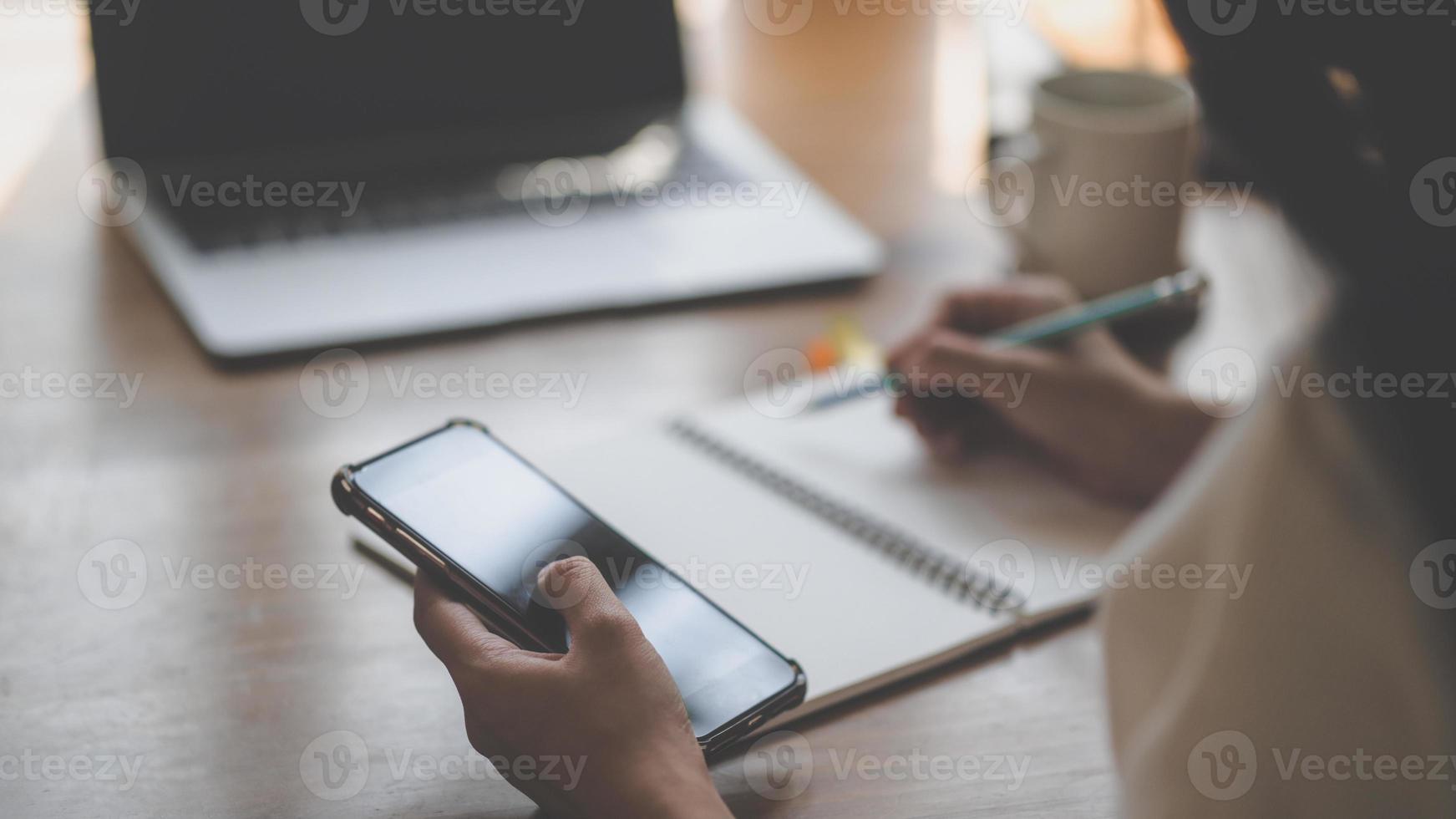 A young woman uses a smartphone and writes in a notebook. photo