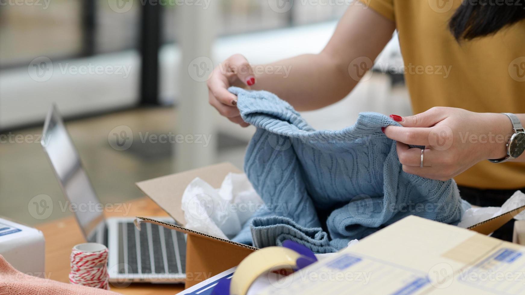 Online selling woman packing sweaters in boxes for delivery. photo