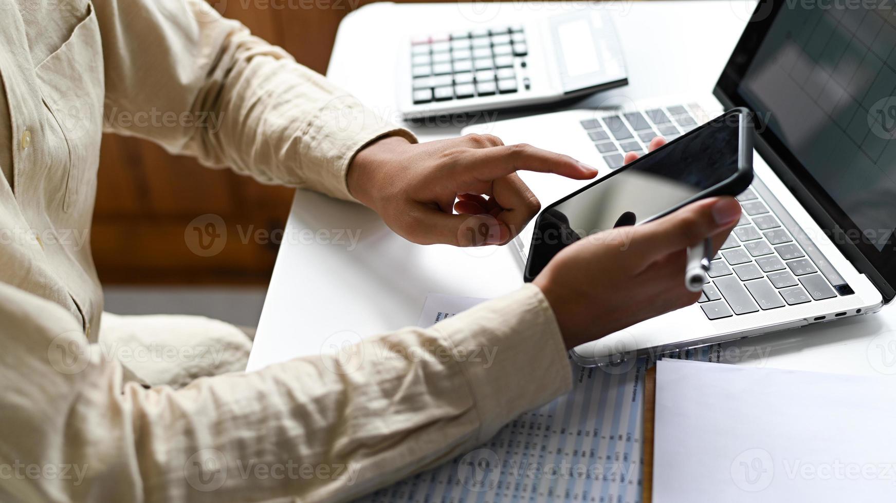 Hand operates a smartphone with a laptop and graphs. photo