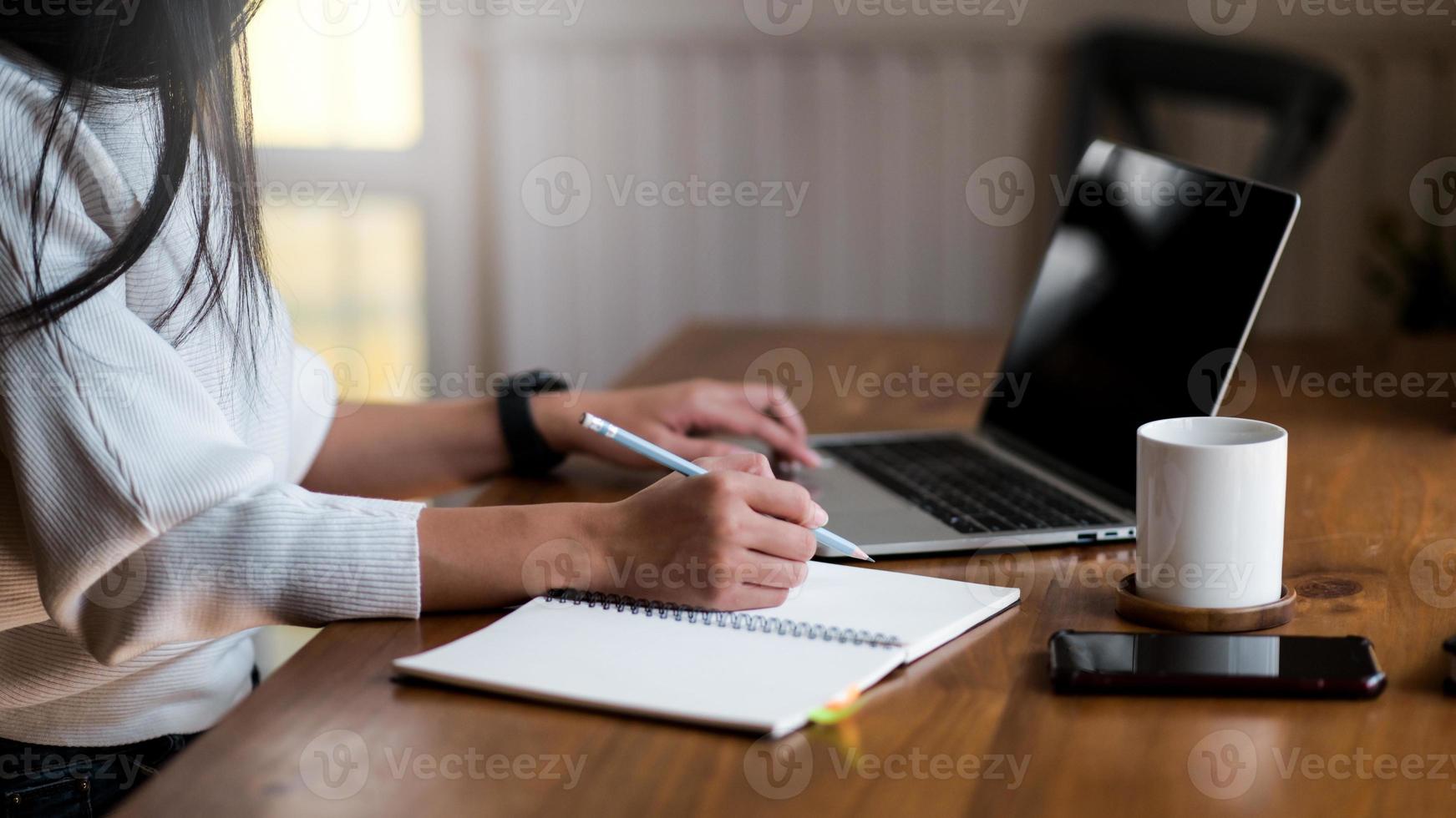 Young woman works from home, she uses a laptop and takes notes. photo