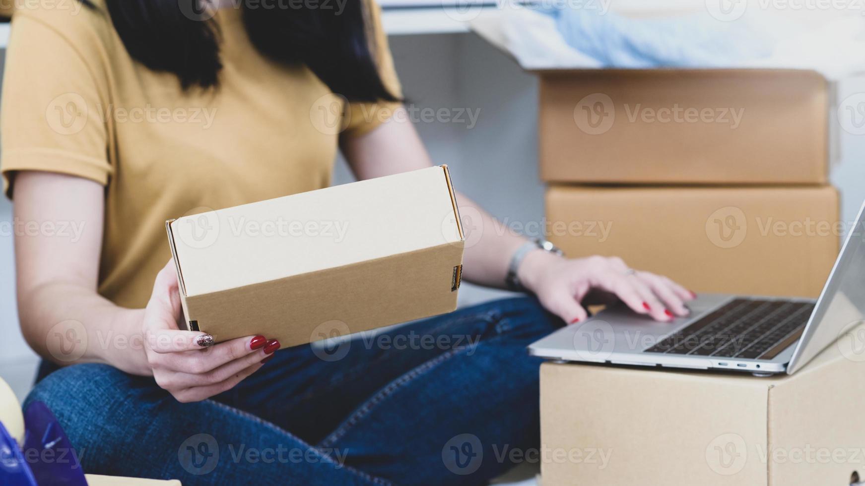 mujer sosteniendo cajas de paquetería y usando laptop, vendiendo productos en línea. foto