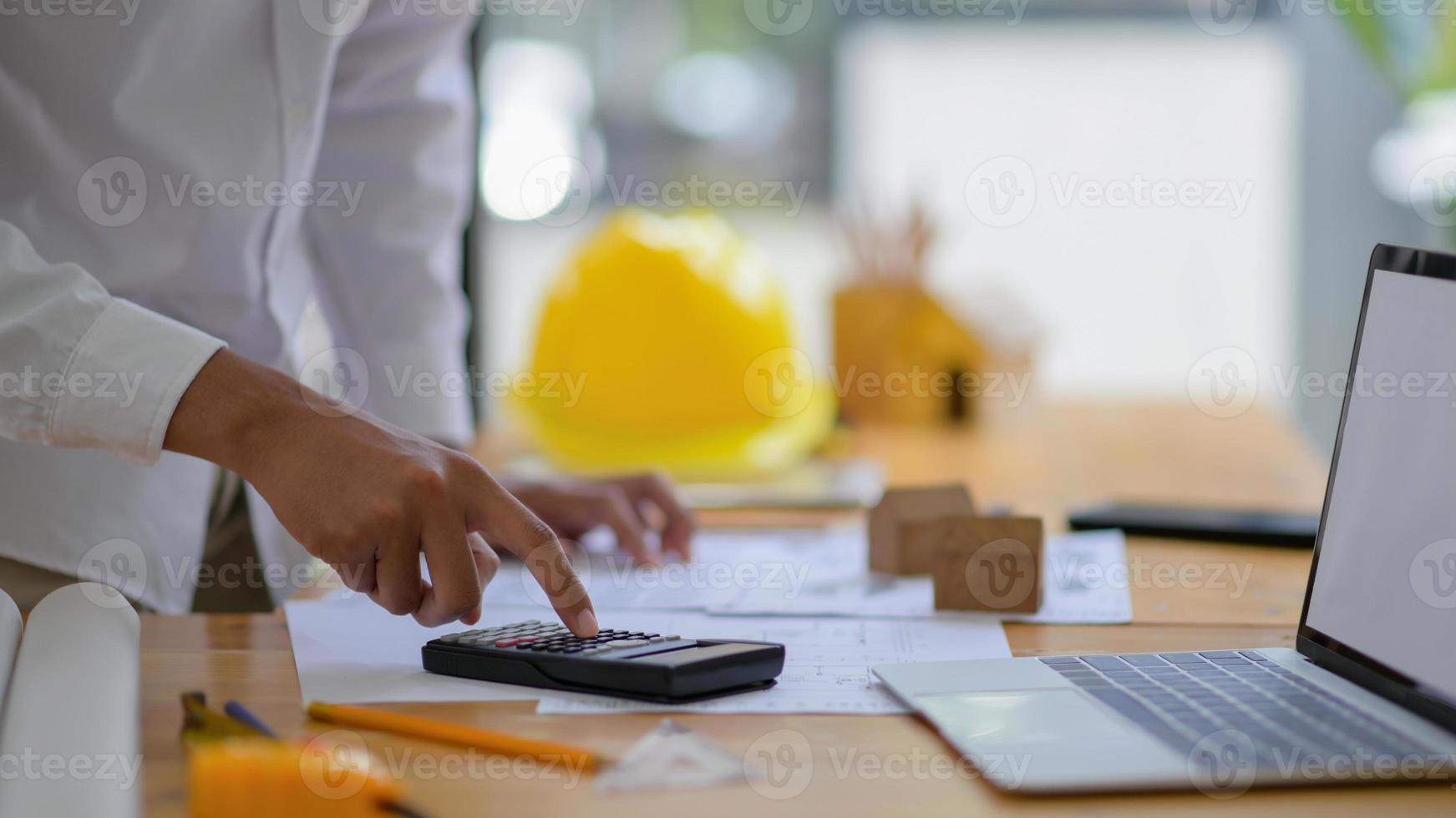 joven ingeniero está utilizando una calculadora para calcular los planos de la casa. foto