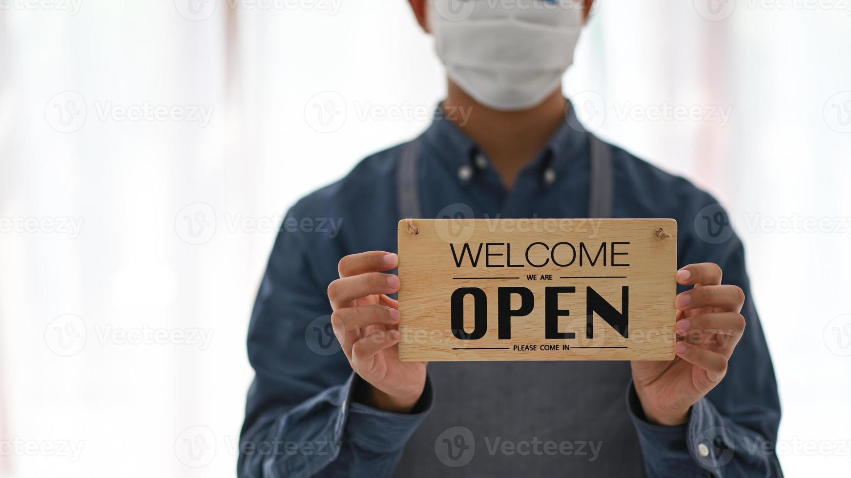 A young man wearing a mask holds an Open sign to open the service. photo
