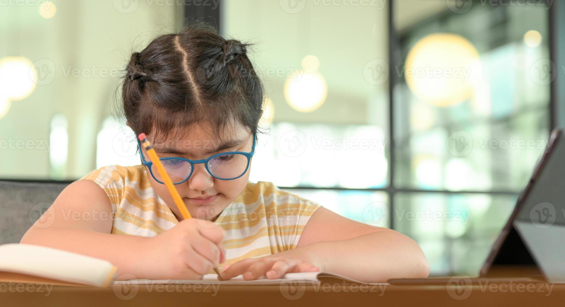 Child girl with glasses is studying at home with serious expression. photo