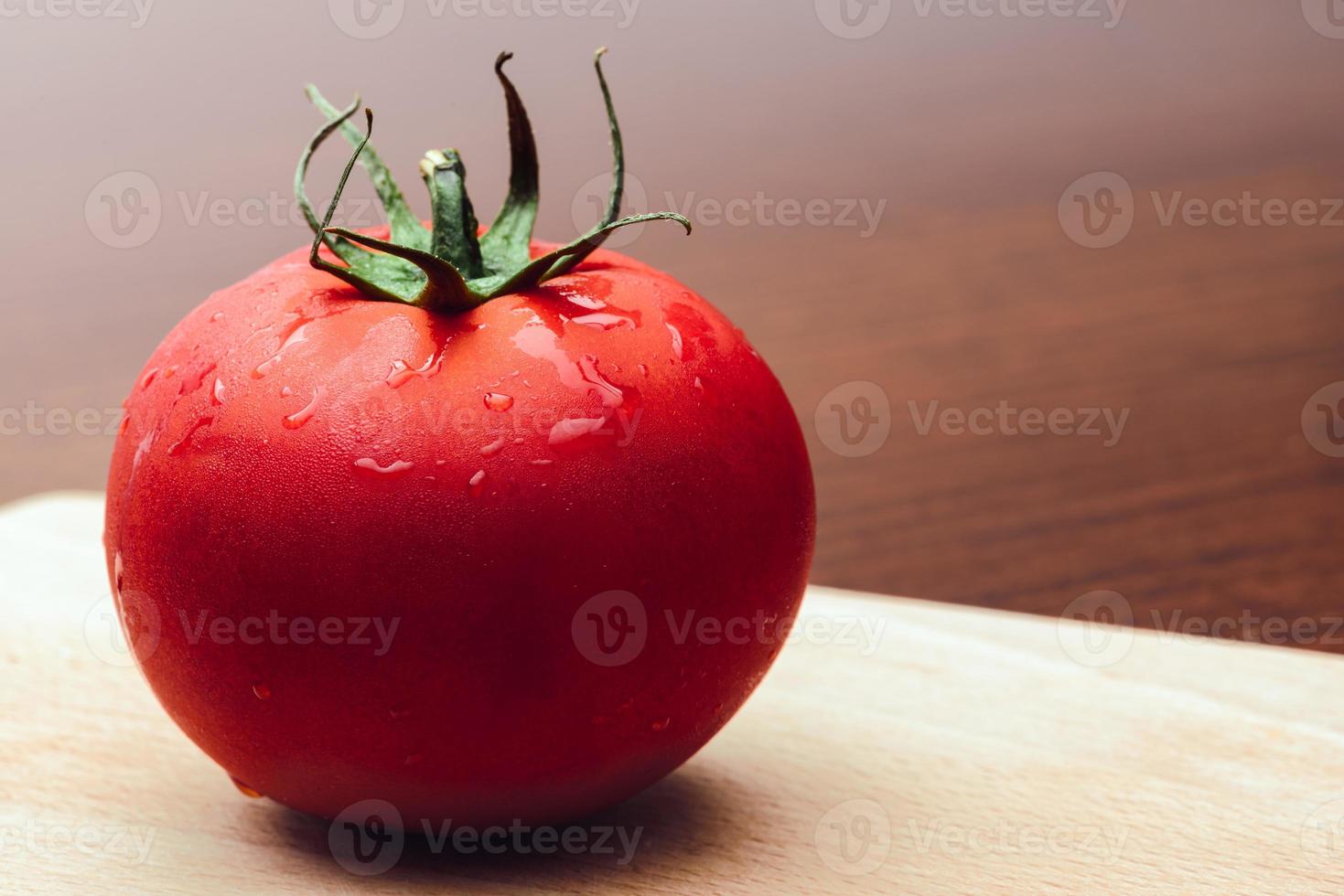 Red tomato on a cutting board on the wooden background. Copy space. Fresh tomato for cooking. Tomato with droplets of water. photo