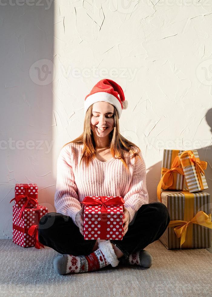 Mujer joven con gorro de Papá Noel rodeado de regalos foto