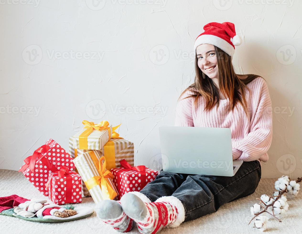 Mujer joven con gorro de Papá Noel de compras online rodeado de regalos foto