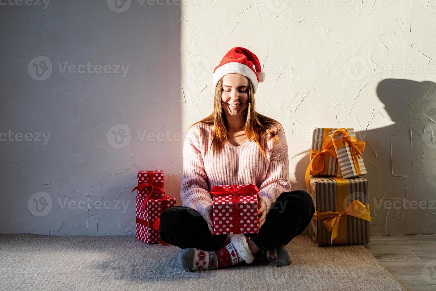 Mujer joven con gorro de Papá Noel rodeado de regalos foto