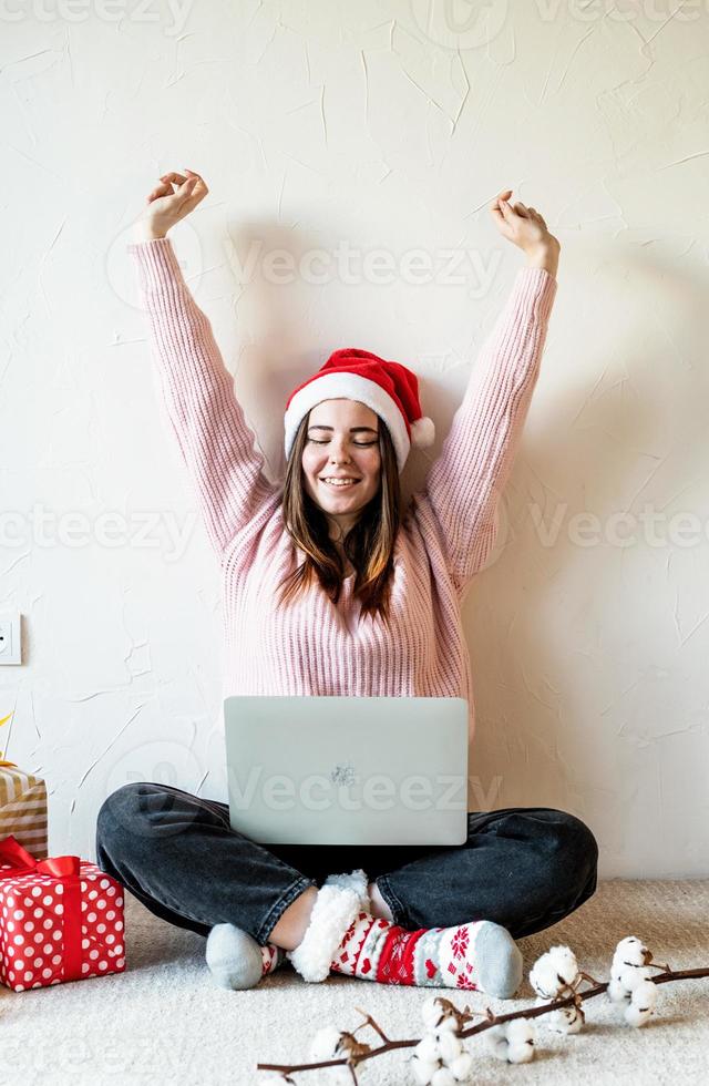 Mujer joven con gorro de Papá Noel de compras online rodeado de regalos foto