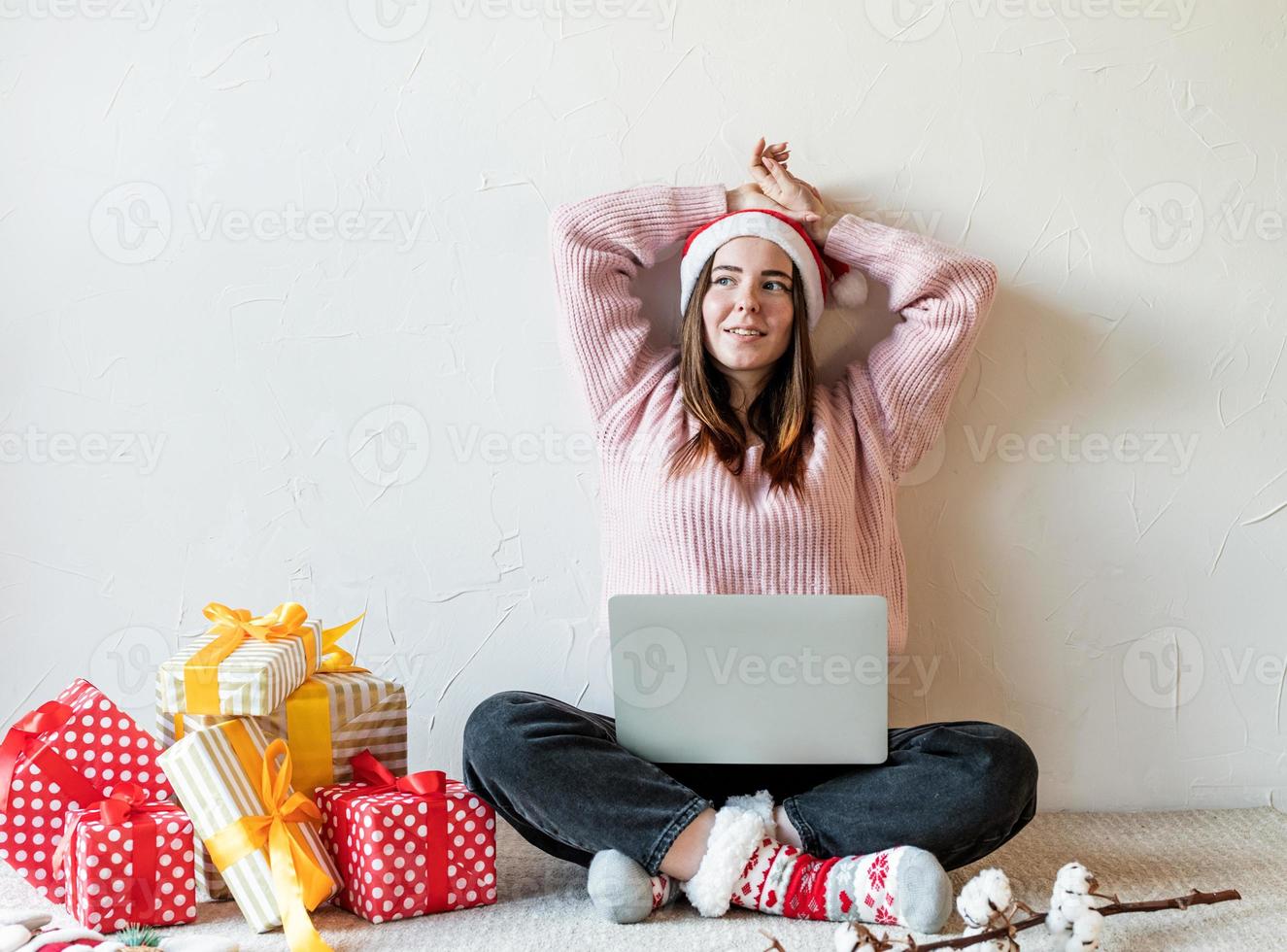 Mujer joven con gorro de Papá Noel de compras online rodeado de regalos foto