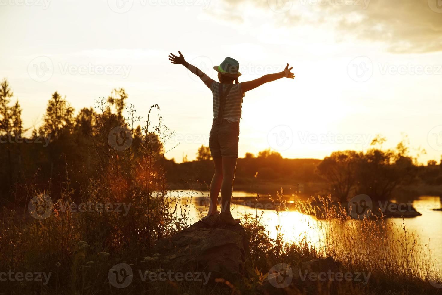 Happy girl standing on a rock at sunset photo