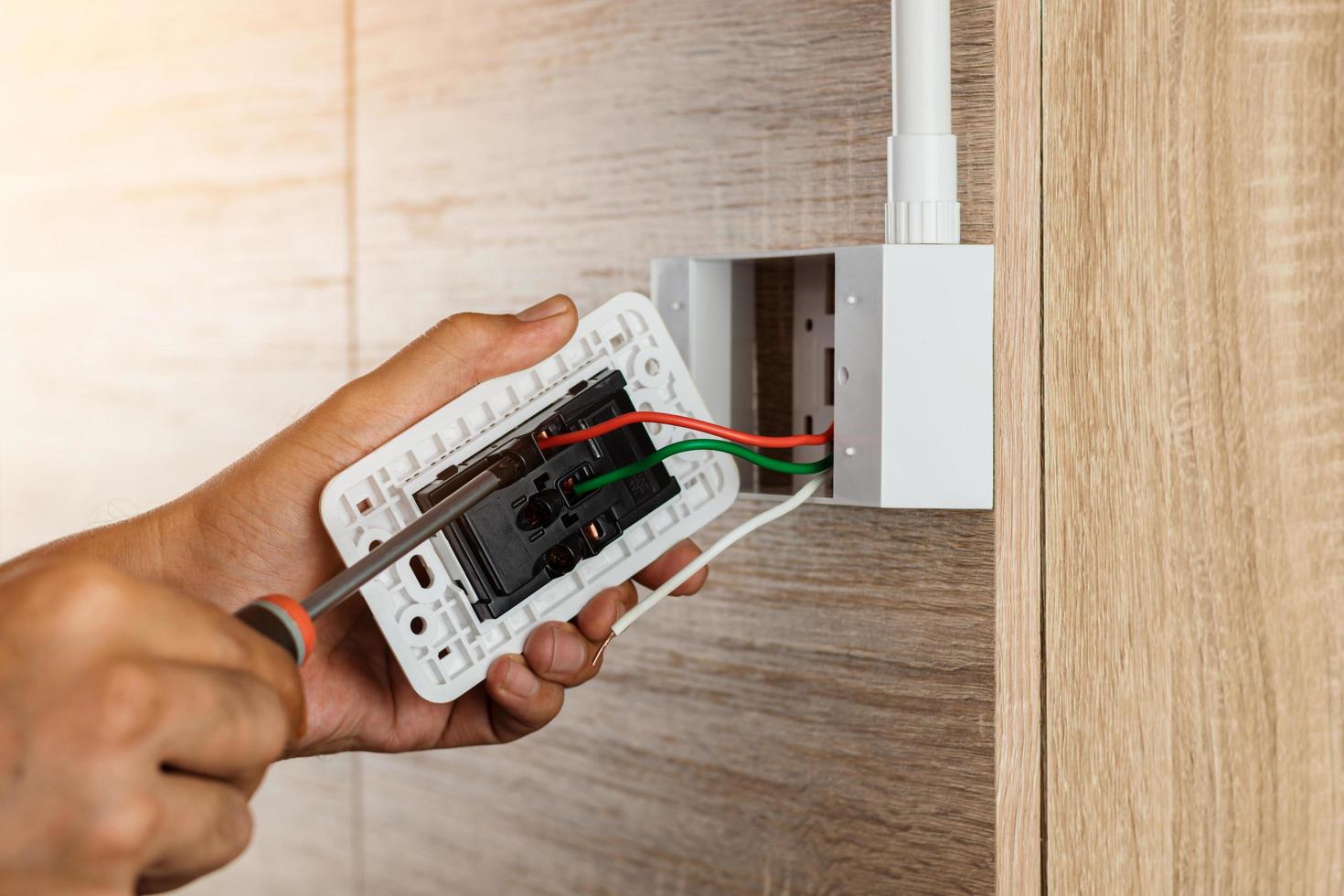 Hand of an electrician is using a screwdriver to attach the wires to the socket. photo