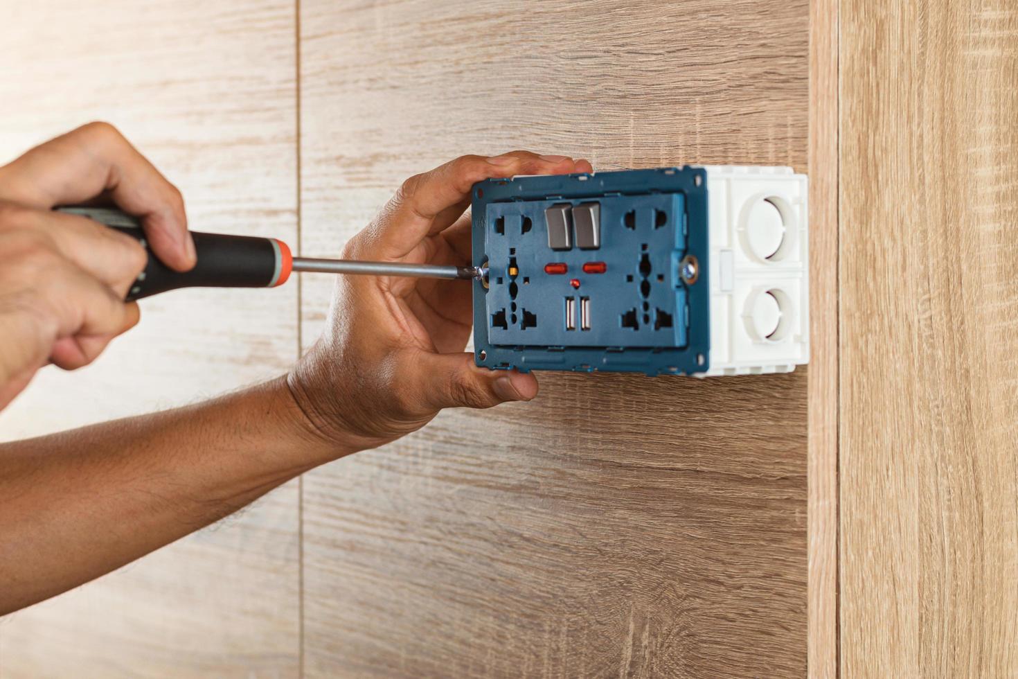 Electrician is using a screwdriver to install a power outlet in to a plastic box on a wooden wall. photo