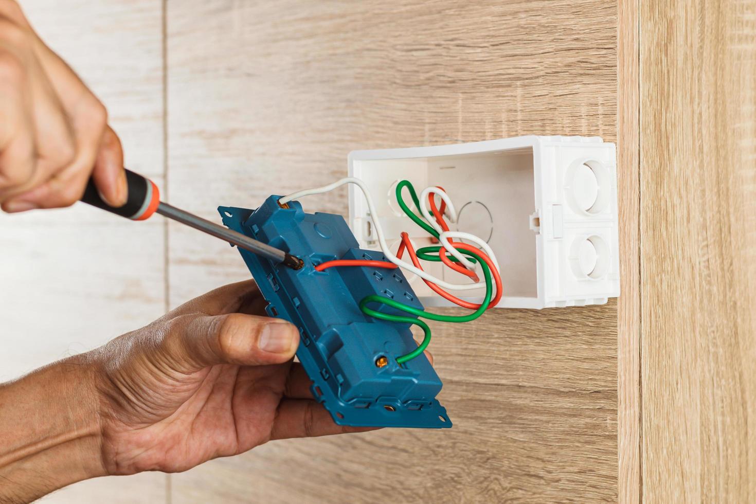 Hand of an electrician is using a screwdriver to attach the wires to the socket. photo